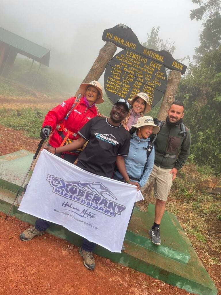 Climbers and an Exuberant team member at Lemosho Gate holding the company banner.