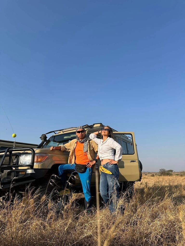 Two travellers beside a safari vehicle in Tanzania’s grasslands.